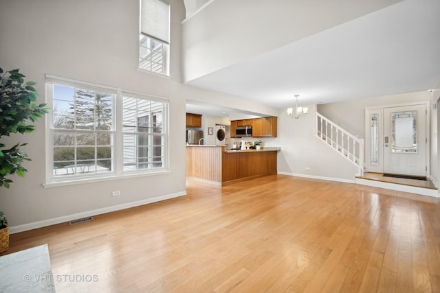 unfurnished living room featuring visible vents, light wood-style flooring, a high ceiling, an inviting chandelier, and baseboards