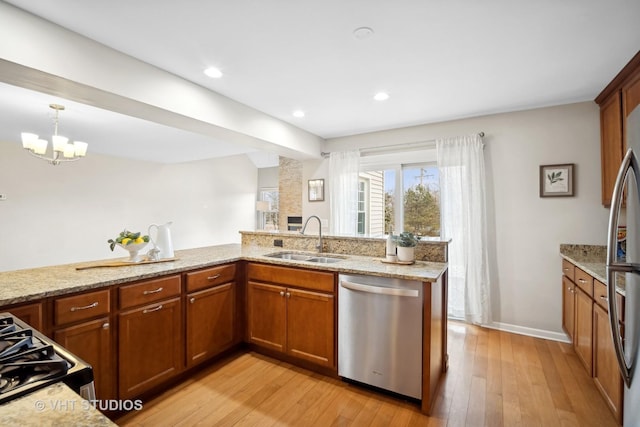 kitchen with light wood finished floors, brown cabinets, light stone countertops, stainless steel appliances, and a sink