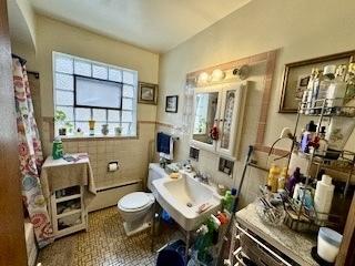 bathroom with tile walls, baseboard heating, a shower with shower curtain, toilet, and wainscoting