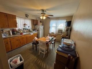 kitchen with freestanding refrigerator, brown cabinetry, light countertops, and a ceiling fan