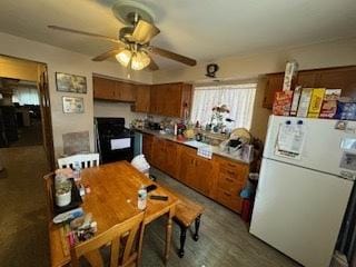 kitchen featuring brown cabinetry, gas range oven, freestanding refrigerator, and a ceiling fan