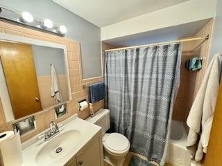 bathroom with tile walls, vanity, toilet, and shower / bathtub combination with curtain