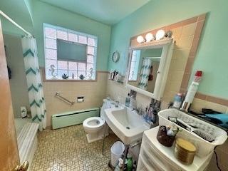 full bathroom featuring toilet, a baseboard radiator, tile walls, and a sink