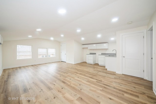 unfurnished living room featuring lofted ceiling, a sink, recessed lighting, light wood-style floors, and baseboards