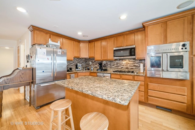 kitchen featuring a kitchen bar, a kitchen island, tasteful backsplash, stainless steel appliances, and light wood-style floors