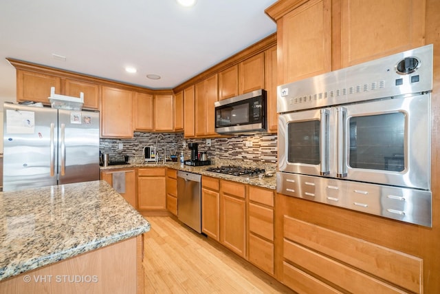 kitchen featuring light stone countertops, light wood-style floors, tasteful backsplash, and appliances with stainless steel finishes