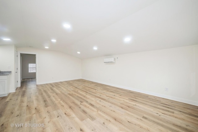 empty room featuring a wall unit AC, baseboards, lofted ceiling, recessed lighting, and light wood-type flooring