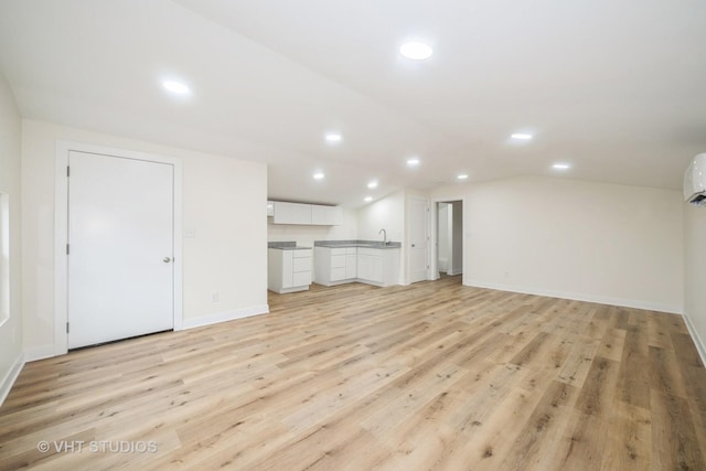 unfurnished living room featuring vaulted ceiling, recessed lighting, light wood finished floors, and a sink