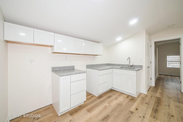 kitchen featuring light stone counters, white cabinetry, light wood-style floors, and a sink