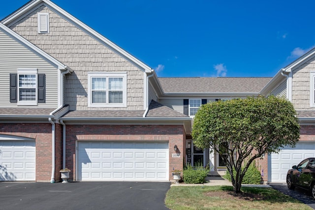 view of property with brick siding, an attached garage, driveway, and roof with shingles