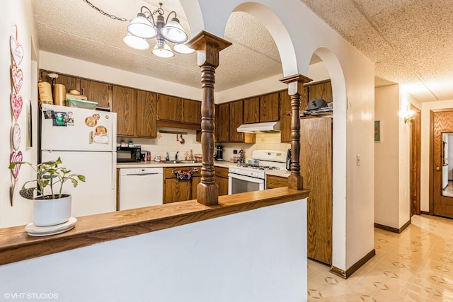 kitchen featuring under cabinet range hood, a peninsula, white appliances, baseboards, and tasteful backsplash