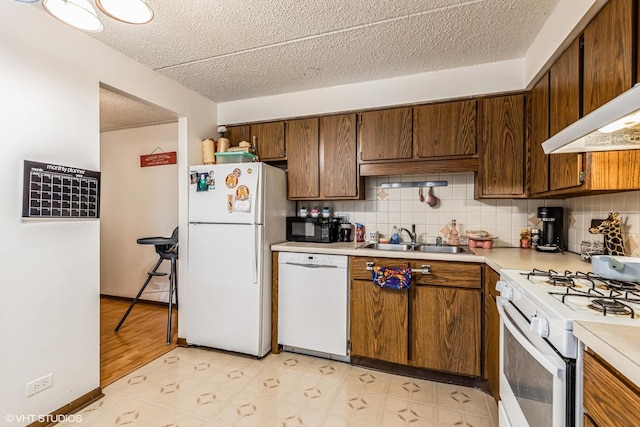 kitchen featuring white appliances, a sink, light countertops, decorative backsplash, and light floors