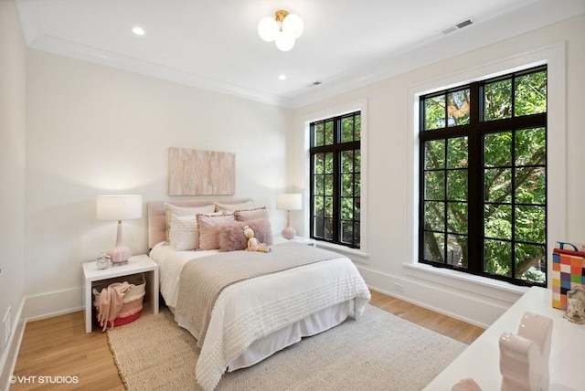 bedroom with visible vents, baseboards, ornamental molding, and light wood finished floors