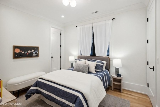 bedroom with baseboards, visible vents, light wood finished floors, and ornamental molding