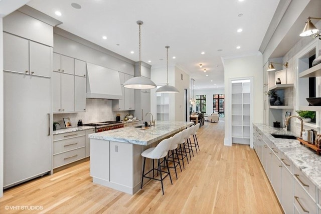 kitchen featuring paneled fridge, light wood-type flooring, a large island with sink, and custom range hood