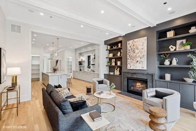 living room with built in shelves, visible vents, light wood finished floors, beam ceiling, and crown molding