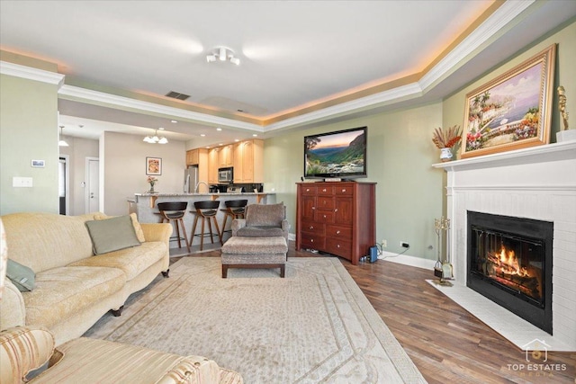 living area with dark wood-style floors, visible vents, a fireplace with flush hearth, ornamental molding, and baseboards