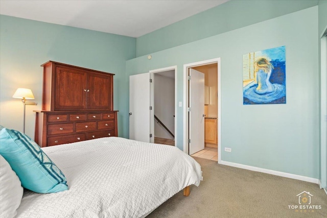 bedroom featuring vaulted ceiling, baseboards, ensuite bathroom, and light colored carpet