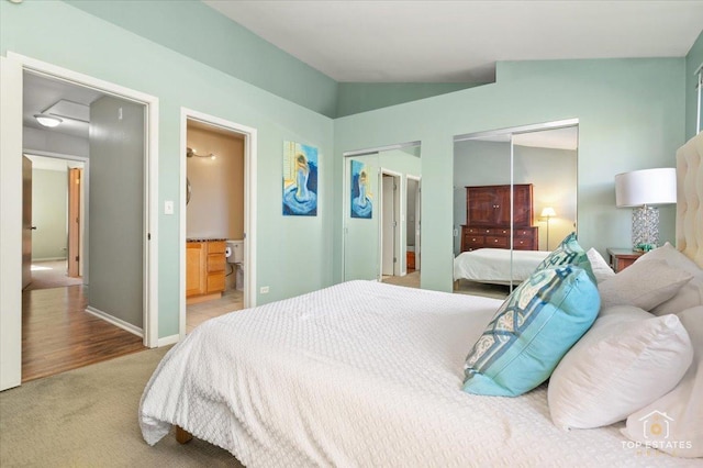 bedroom with carpet floors, two closets, lofted ceiling, ensuite bathroom, and baseboards