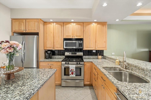 kitchen featuring light brown cabinetry, appliances with stainless steel finishes, a sink, and light stone countertops