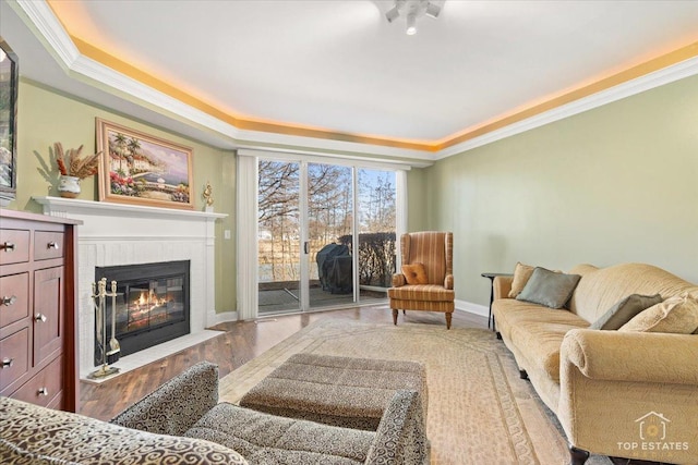 living room featuring a fireplace with flush hearth, crown molding, baseboards, and wood finished floors