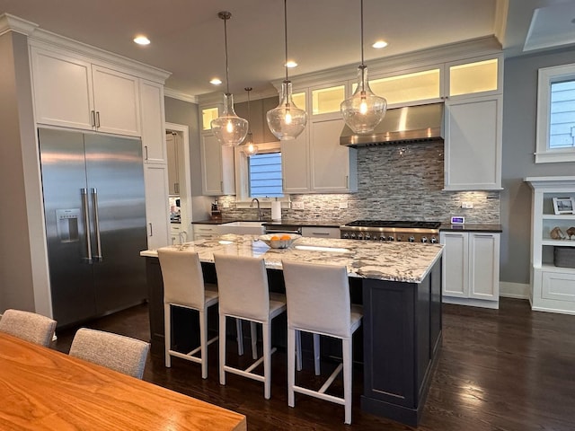 kitchen featuring tasteful backsplash, stove, a center island, built in refrigerator, and wall chimney range hood