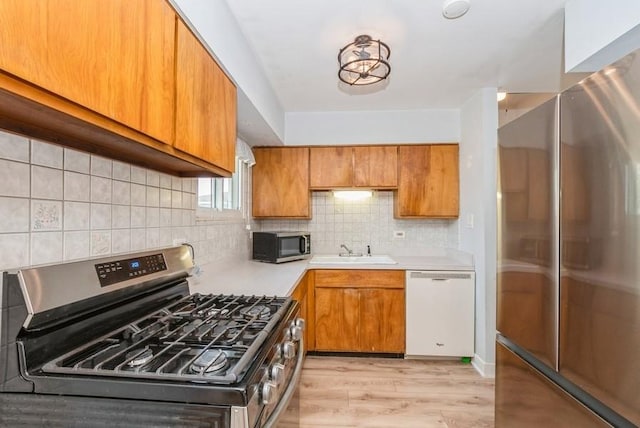 kitchen featuring light wood finished floors, light countertops, appliances with stainless steel finishes, brown cabinetry, and a sink