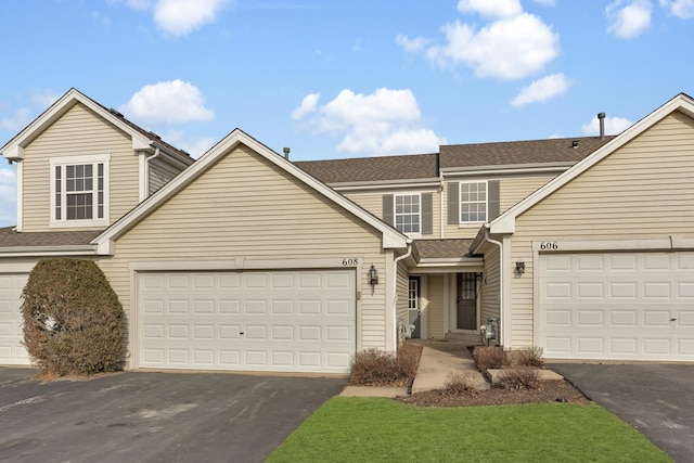 traditional-style house featuring an attached garage, a shingled roof, and aphalt driveway