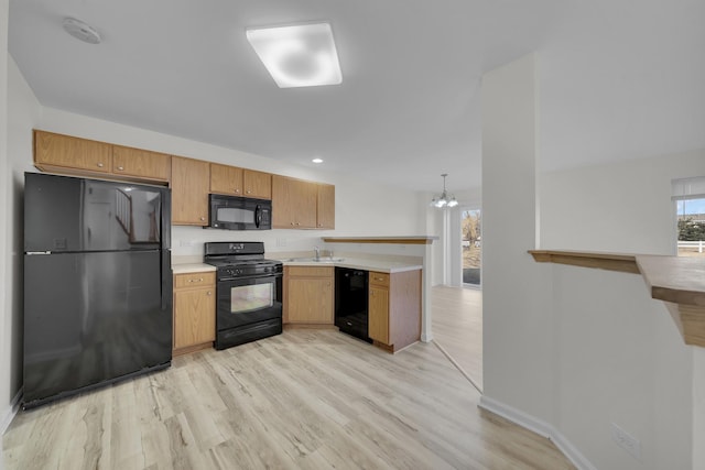 kitchen with light countertops, light wood-style flooring, an inviting chandelier, a peninsula, and black appliances