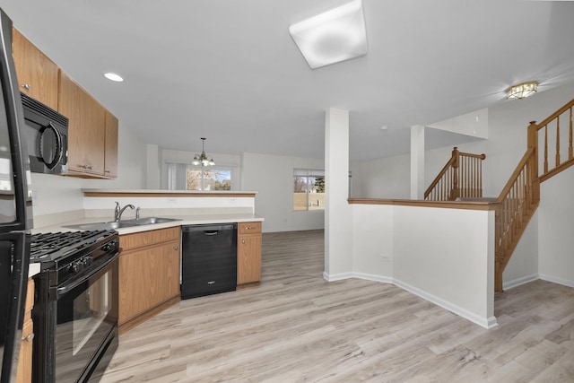 kitchen with a peninsula, black appliances, light wood-style flooring, and light countertops