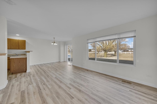 unfurnished living room with a sink, visible vents, baseboards, light wood-style floors, and an inviting chandelier