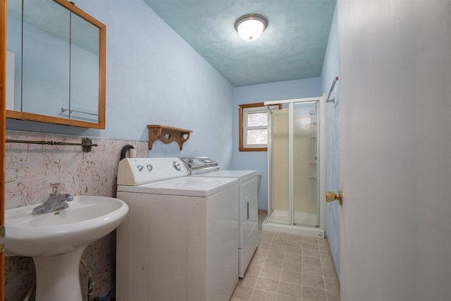 clothes washing area with light tile patterned flooring, a wainscoted wall, laundry area, a sink, and washer and clothes dryer