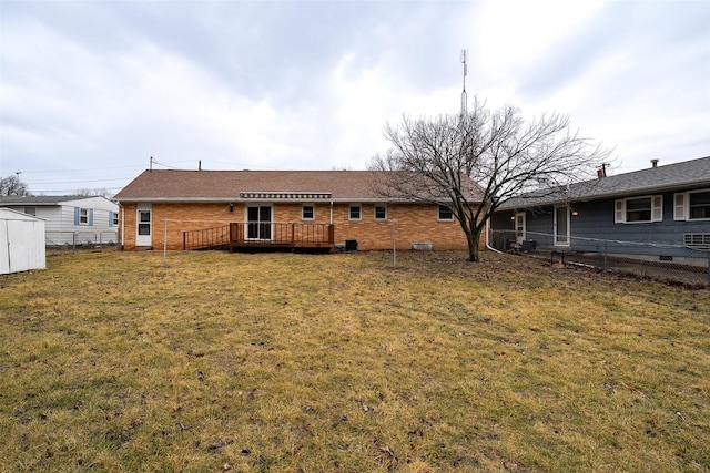 rear view of house with brick siding, a yard, a wooden deck, and fence