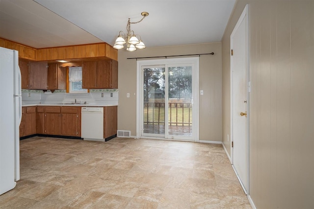 kitchen with white appliances, brown cabinetry, an inviting chandelier, light countertops, and a sink