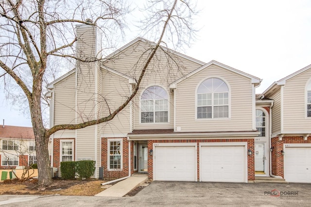 view of property with an attached garage, a chimney, aphalt driveway, and brick siding