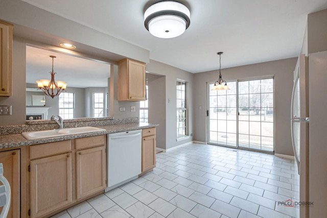 kitchen with white appliances, light brown cabinets, a sink, and decorative light fixtures