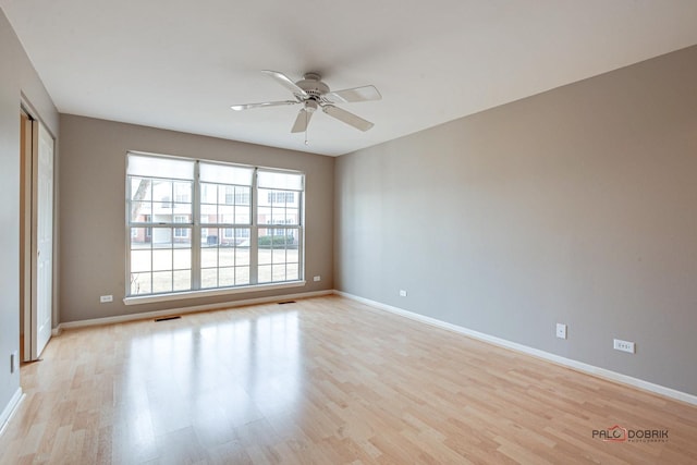 empty room featuring a ceiling fan, light wood-type flooring, visible vents, and baseboards