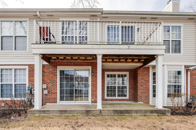 back of property with brick siding and a balcony