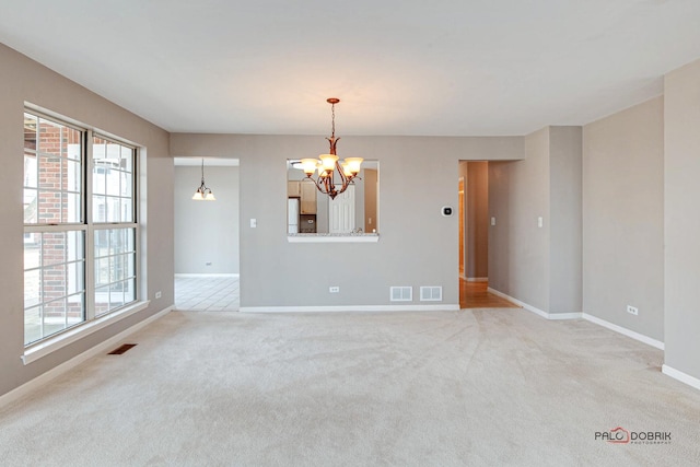 carpeted empty room featuring an inviting chandelier, plenty of natural light, and visible vents