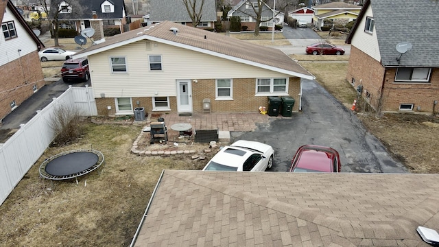 rear view of property featuring central air condition unit, a fenced backyard, a residential view, and brick siding