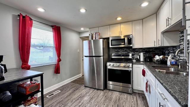 kitchen featuring stainless steel appliances, a sink, white cabinetry, light wood-style floors, and decorative backsplash