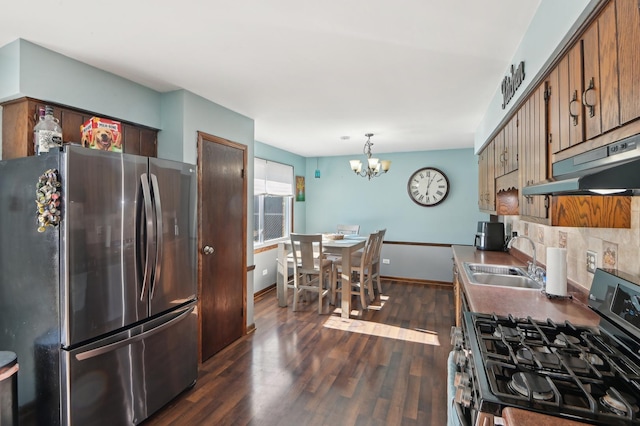 kitchen with dark wood-style floors, a sink, decorative backsplash, under cabinet range hood, and appliances with stainless steel finishes