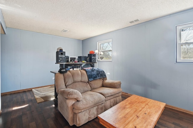 living room featuring visible vents, plenty of natural light, a textured ceiling, and dark wood-type flooring