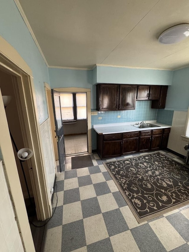 kitchen with dark brown cabinetry, dark floors, light countertops, crown molding, and a sink