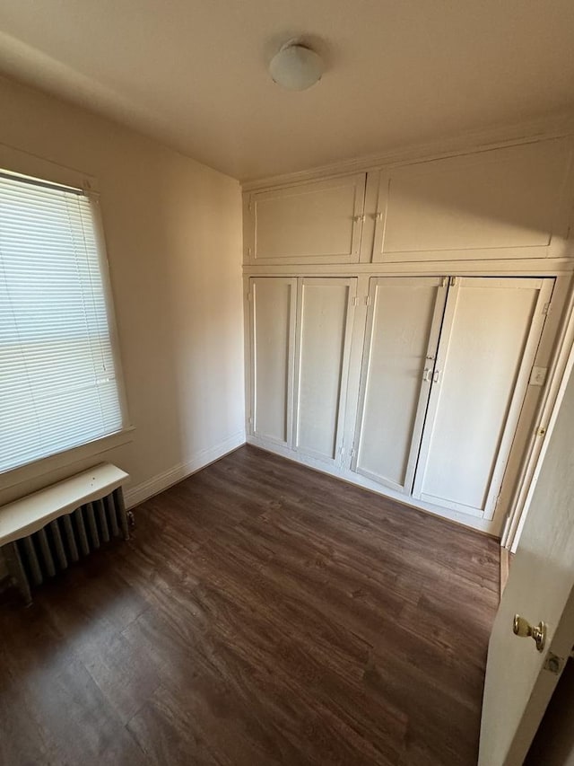 unfurnished bedroom featuring radiator heating unit, a closet, baseboards, and dark wood-style flooring