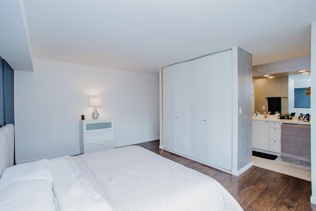 bedroom featuring a closet, baseboards, ensuite bath, and wood finished floors