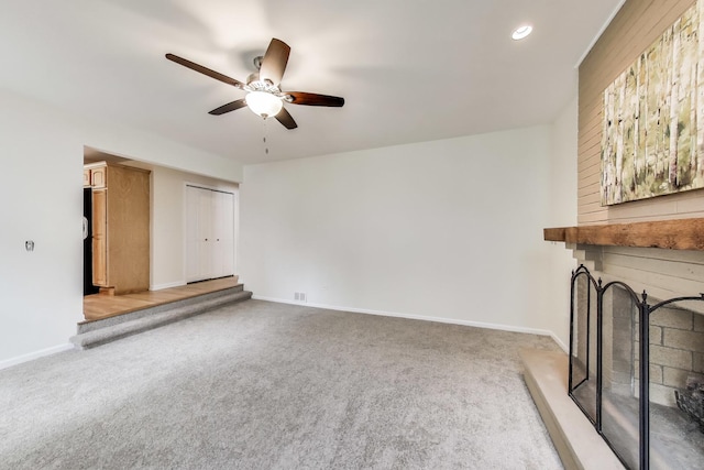 unfurnished living room featuring light carpet, a fireplace with raised hearth, a ceiling fan, recessed lighting, and baseboards