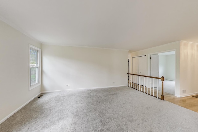carpeted empty room featuring visible vents, ornamental molding, and baseboards