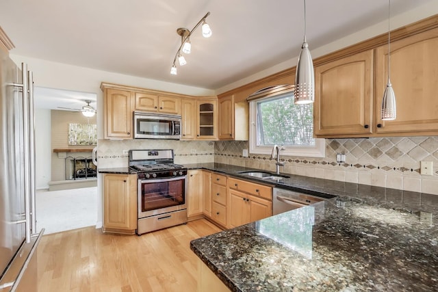 kitchen featuring appliances with stainless steel finishes, a sink, light wood finished floors, dark stone countertops, and decorative backsplash