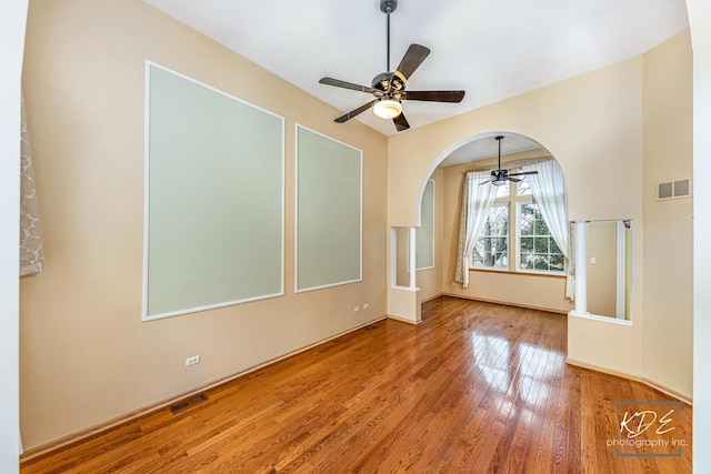 unfurnished room with arched walkways, visible vents, ceiling fan, and hardwood / wood-style flooring